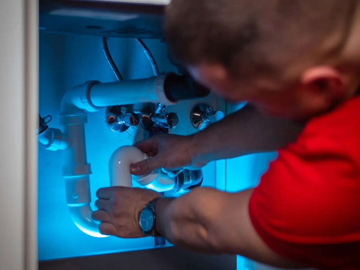 A plumber fitting a drain trap under a kitchen sink