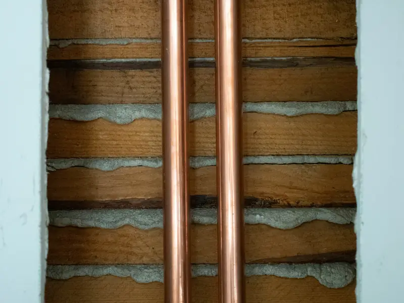 Two copper water lines running up through an opened wall