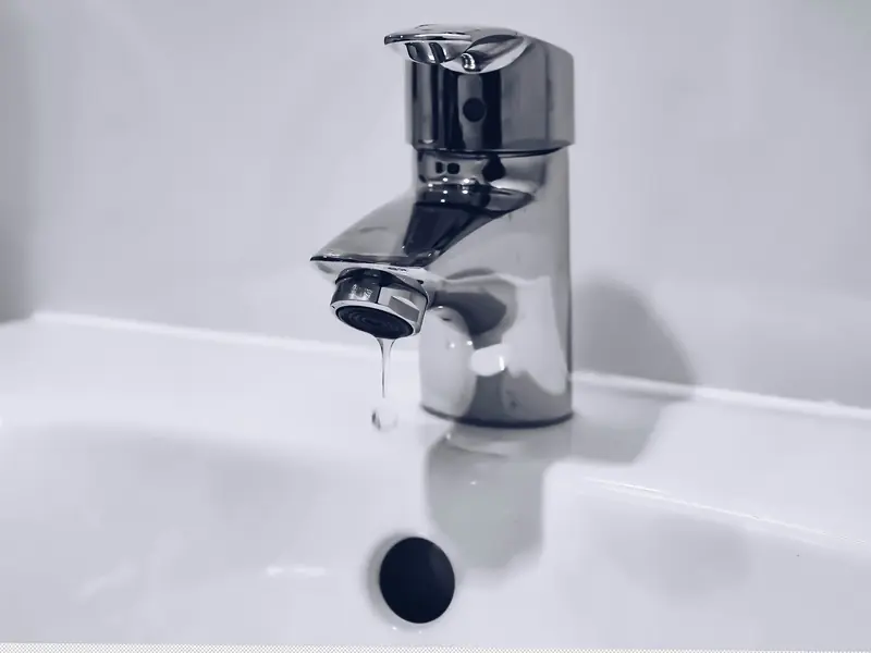 A bathroom faucet with a drip falling into the sink