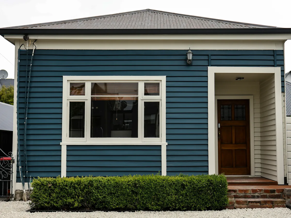 A blue clapboard house with cream window trim and a wood front door