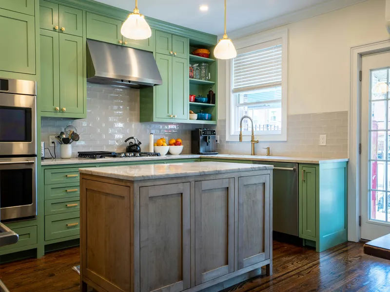 A kitchen with sage green painted cabinets and a stained wood island