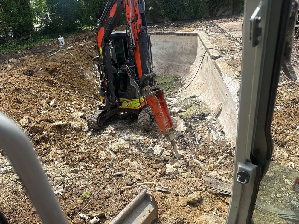 Excavator with hydraulic breaker demolishing a pool