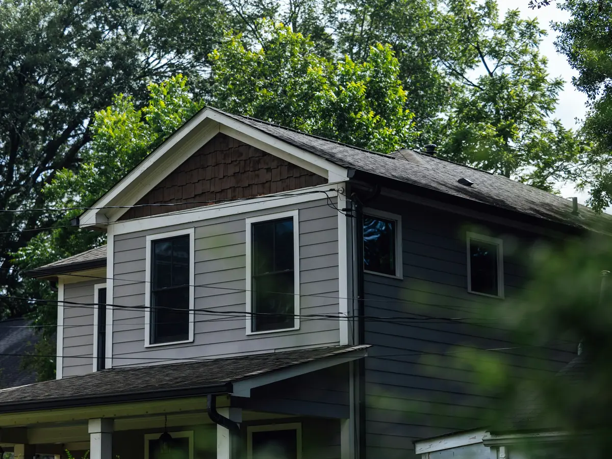 Two-story house with gray lap siding under tall shade trees