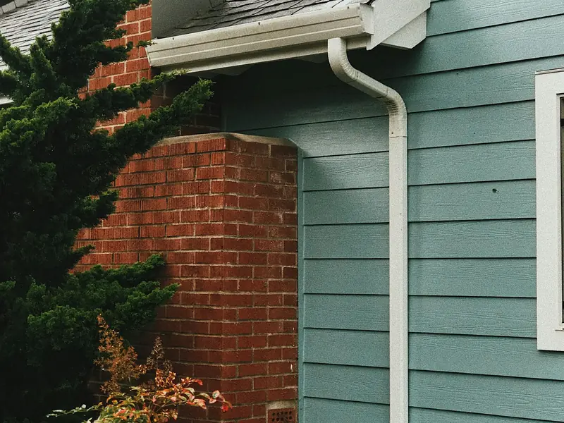 Painted lap siding with a white gutter and downspout beside a brick chimney