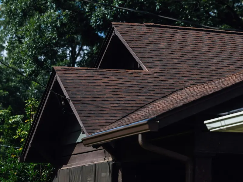 Brown shingle roof where two gables meet, with capped ridges and a gutter along the eave