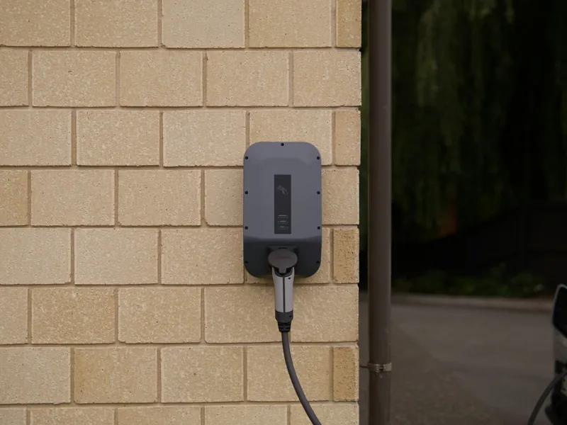 An EV charger mounted on a brick wall with the cable plugged in