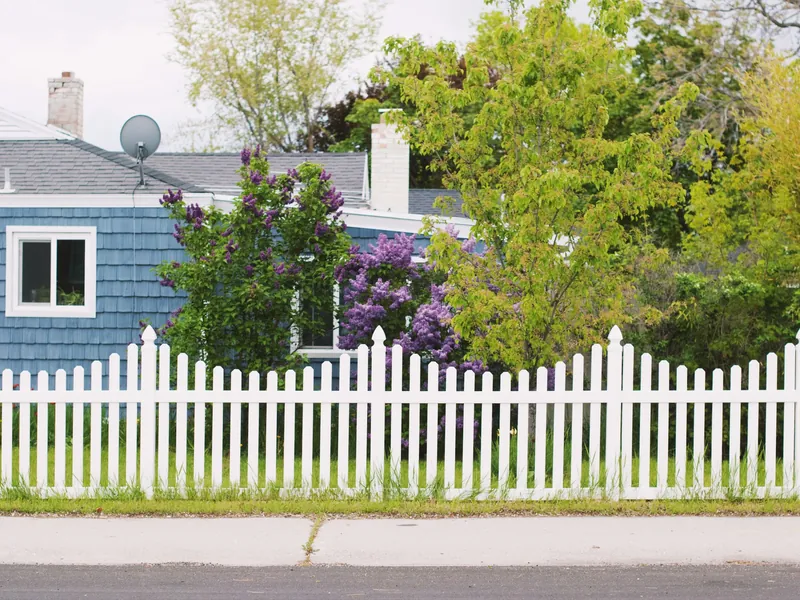 A white picket fence along the front yard of a blue house