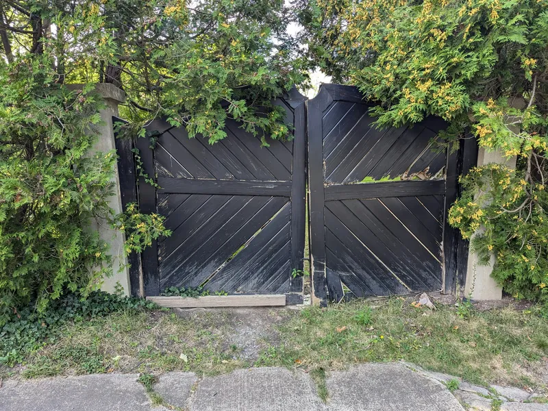 A weathered black double gate with a broken board, before repair